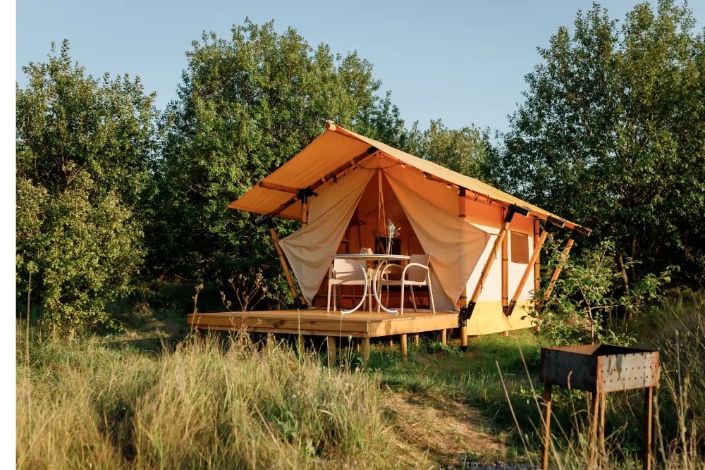 Открытая уютная глэмпинг-палатка среди зелени — для тихого отдыха на природе.