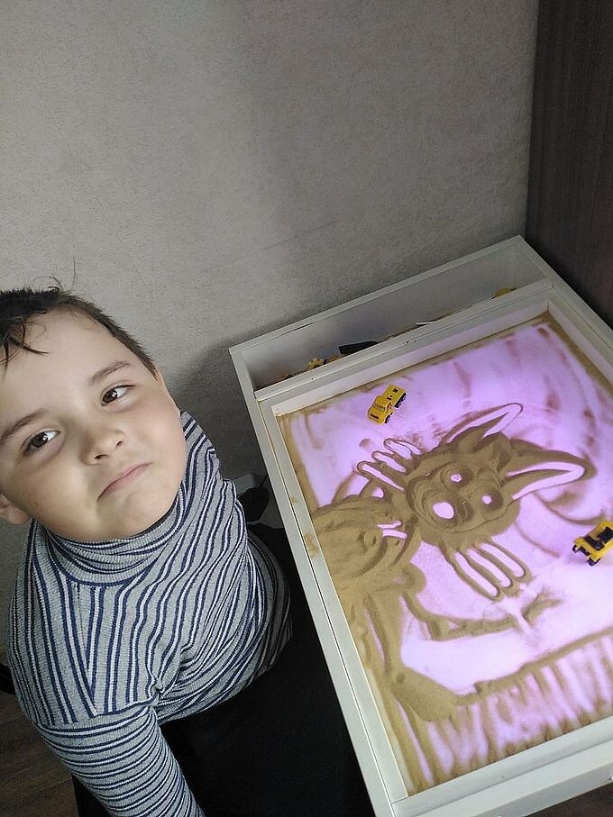 Мальчик нарисовал руками на песке рисунок кота