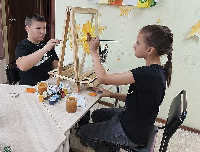 Мальчик и девочка рисуют на прозрачном мольберте