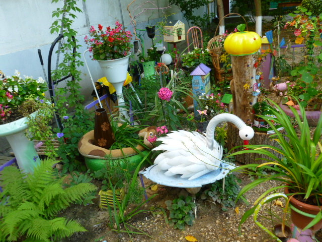 Здесь нет целостного сюжета, есть миникадры: домики, лебеди, кашпо с цветами, Тыквы, игрушки машинки и паровозик. Завораживает яркость, притягивает применимость уже ненужных вещей в общей композиции. Вещи, которые послужили в жизни человека можно применить по-разному, в данном случае в специфическом народном творчестве, стать украшением подъезда, территории около дома.