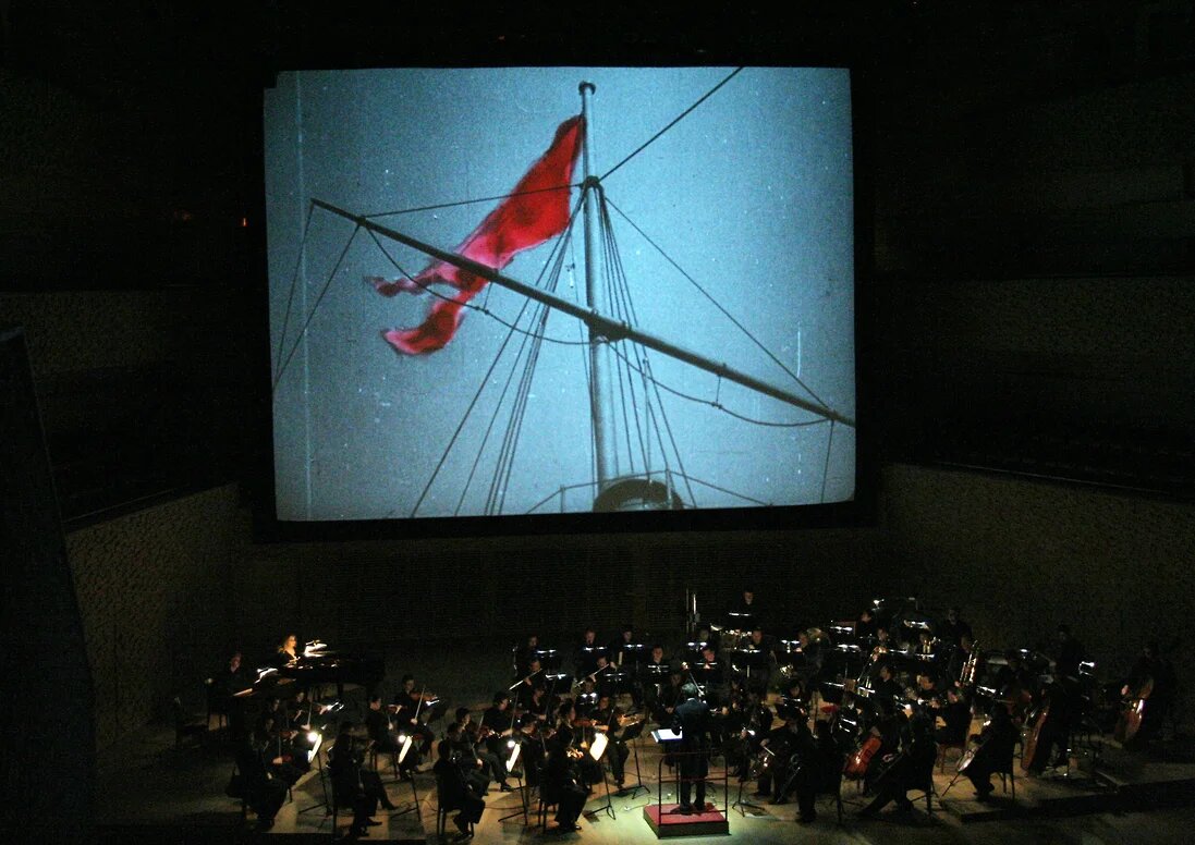 Красный флаг над «Потемкиным» поразил первых зрителей фильма в 1925 году, но в 1905-м мог означать сигнал о готовности к артиллерийской стрельбе, а не к борьбе за счастье трудящихся (на фото — показ отреставрированной ленты, 2008 год. Оригинальную музыку исполняет оркестр Мариинского театра)
Фото: Коммерсантъ / Наташа Разина