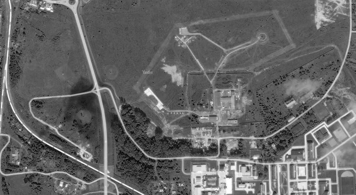 Фотоиллюстрация: Современное фото сайта Яндекс-карты. Пунктирная линия слева - железная дорога маршрута "Калининград - Пионерский". Где-то рядом с пересечением железной дороги и шоссе (в нижней части фото) наш дизель-поезд остановился и мы, толпа призывников, пошли через лес на дорогу, ведущую направо (с резким поворотом вертикально на север). Далее по дугообразной дороге мы вошли на территорию 9-го Флотского экипажа ДКБФ (редкие здания и строевой плац в центре правой части фото). Многоугольник серых полос в центре фото - это взлётно-посадочная полоса и рулёжные дорожки аэродрома базы Нойкурен.