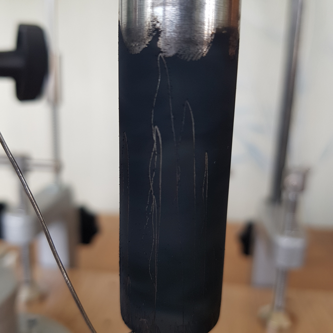 На этом снимке вы видите, как боковую поверхность частично закопченного цилиндра с примыкающей к нему чертилкой, так и оставленный ею след. Который позволяет нам лего определить максимальную степень сжатия пружины после падения на нее этого цилиндра с заданной нами высоты. Так самый большой по высоте пик показывает нам то. что сначала цилиндр отдавал энергию своего движения пружине, сжимая ее. При этом, осталяемый чертилкой след поднимался вверх. После того, как цилиндр полностью передал всю энергию своего движения, сначала произошла очень кратковременная остановка его движения, после которой теперь уже пружина начала передавать ему накопленную ею энергию. А черотилка начала рисовать линию, направленную к основанию цилиндра. После чего, как мы это видим на снимке, произошло еще несколько затухающих афтершоков, и система вернулась в ее исходное состояние.