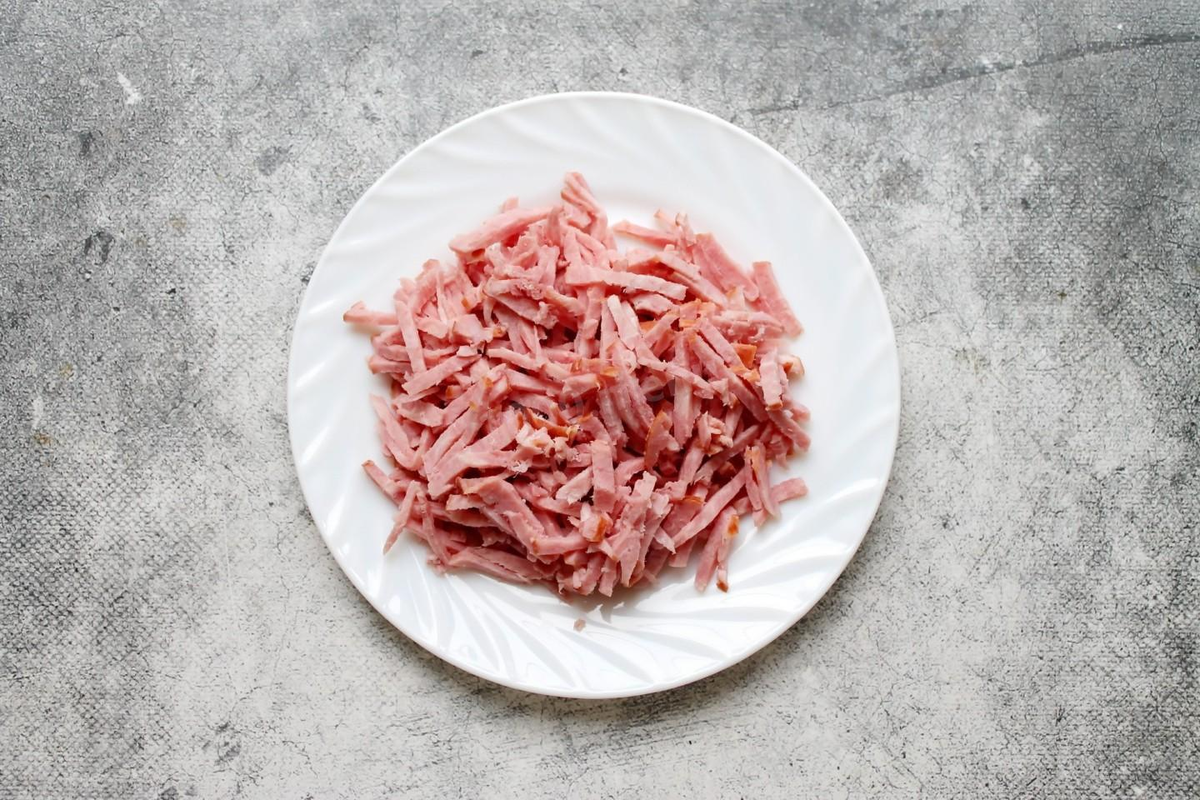 Ветчину порежьте тонкой, короткой соломкой или натрите на крупной терке. Положите ветчину в тарелку. А секреты и тонкости работы с теркой можно узнать в статье под рецептом ниже.