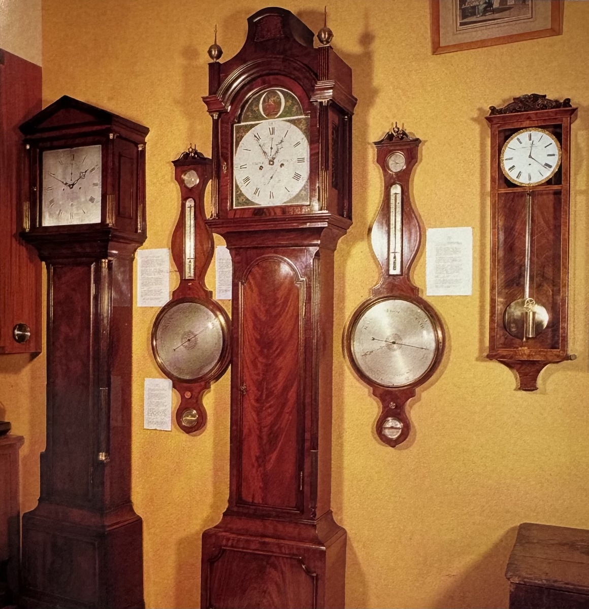 Двое превосходных напольных часов из красного дерева, настенные часы из красного дерева и два барометра. Напольные часы меньших габаритов с архитектурным постаментом с легкой руки аукционеров, хотя и необоснованно, стали называть "бабушкиными" часами. Часы больших размеров с замечательной резьбой по дереву украшены традиционно шарообразными завершающими украшениями со шпилями, однако орнамент из бус вокруг центральной панели шкафчика и на постаменте, а также несколько неуклюжая верхняя часть свидетельствуют о том, что великий век напольных часов клонился к закату. В XIX веке напольные часы в основном не видоизменялись, разве что в последние годы они стали более массивными и появилась дисковая музыкальная шкатулка