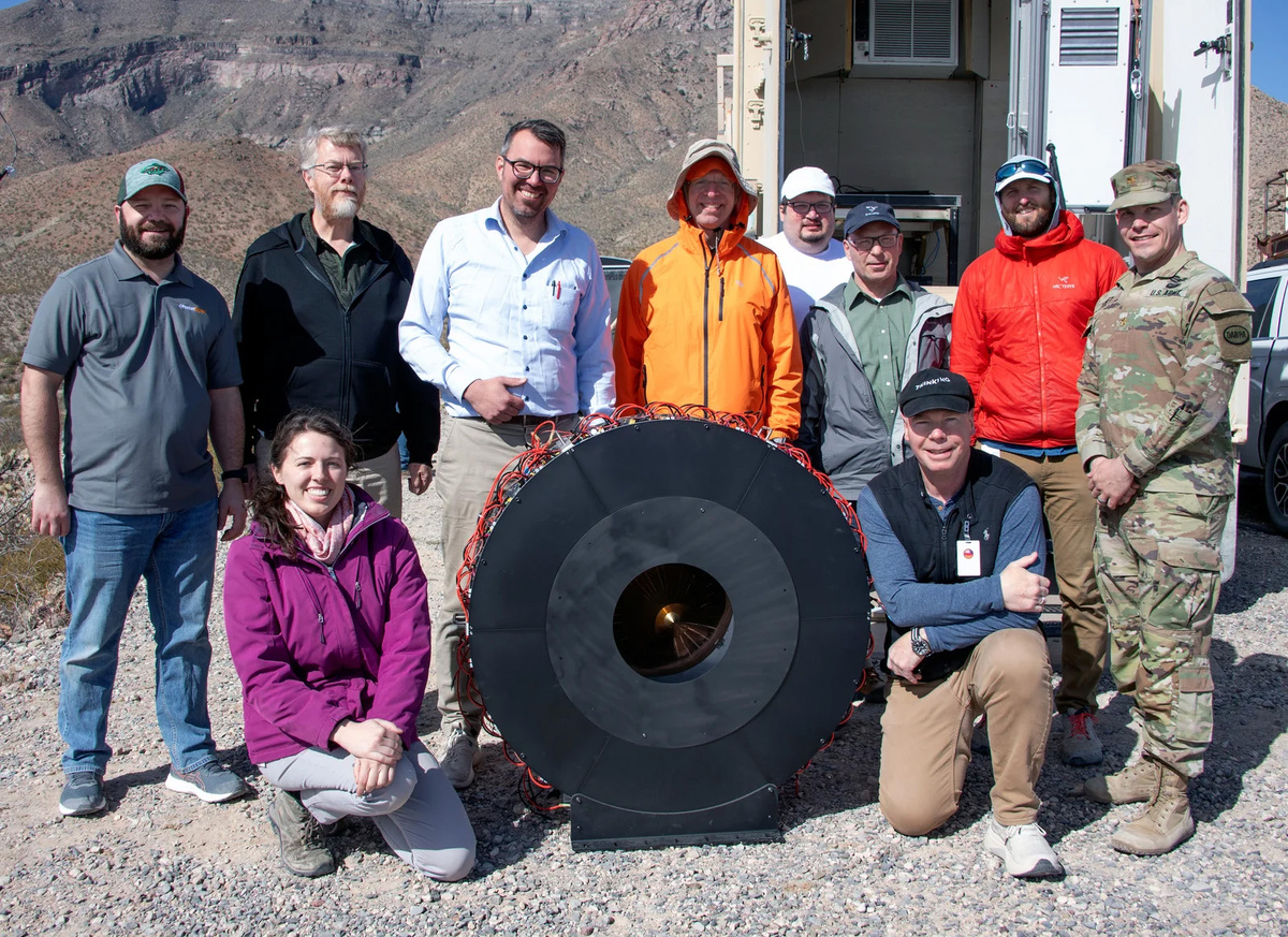 Пол Джаффе (в оранжевом) стоит с демонстрационной командой POWER Receiver Array Demo вокруг ресивера после достижения нового рекорда по беспроводному излучению в испытательном центре высокоэнергетических лазерных систем в Нью-Мексико.Ракетный полигон армии США в Уайт-Сэндс
