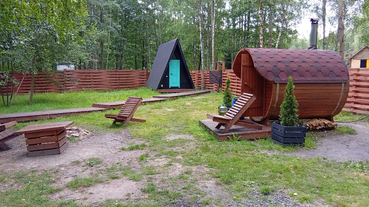 Фиолетовый домик в комплексе Di.Land, июль 2025. Вид от беседки на баню, костровую зону и туалет (у калитки). Фото из личного архива автора.