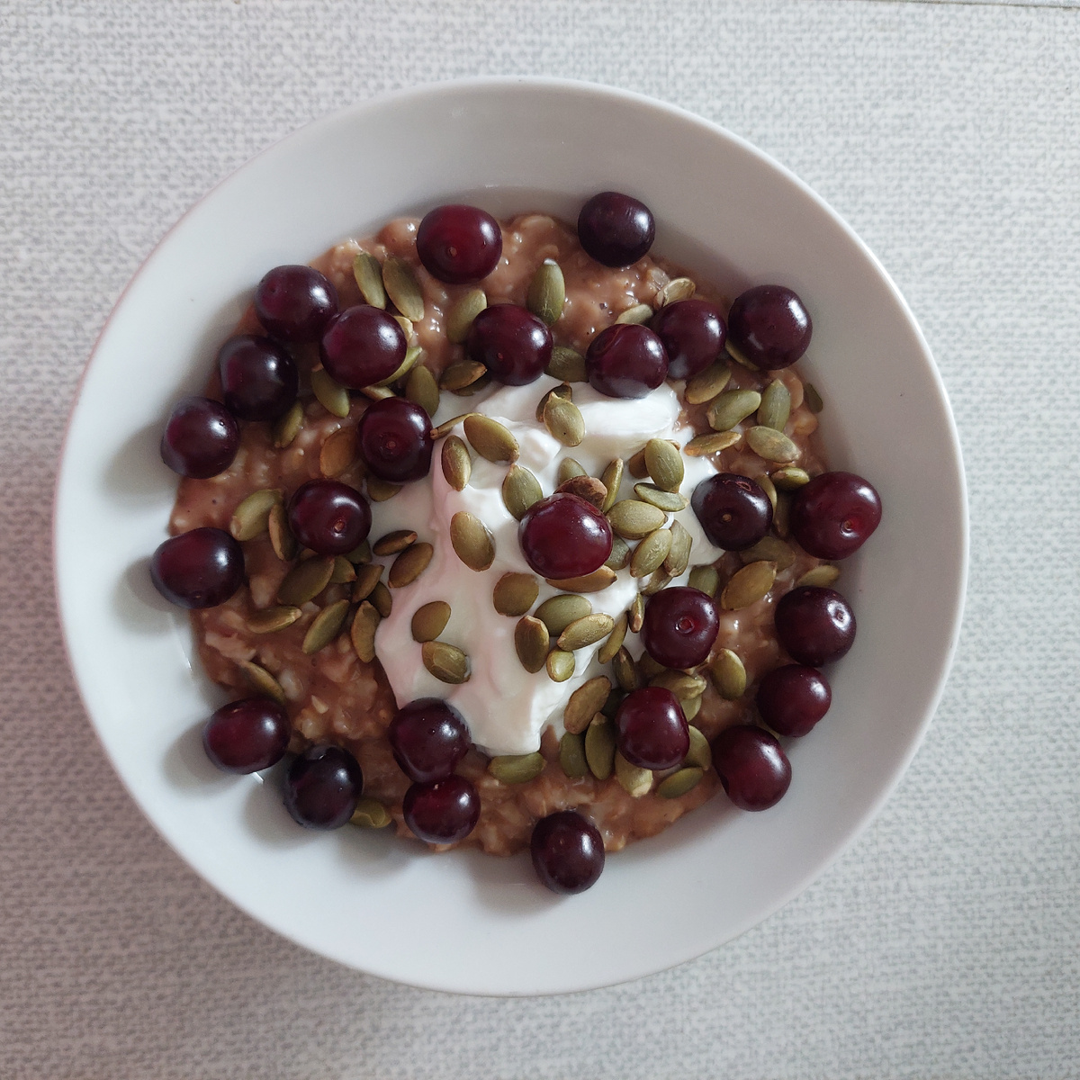 Сварила на воде овсяные хлопья Геркулес традиционный. В тарелку добавила 1 чайную ложку какао, 2 столовые ложки йогурта греческого без добавок, тыквеные семечки и вишню (с дачи).