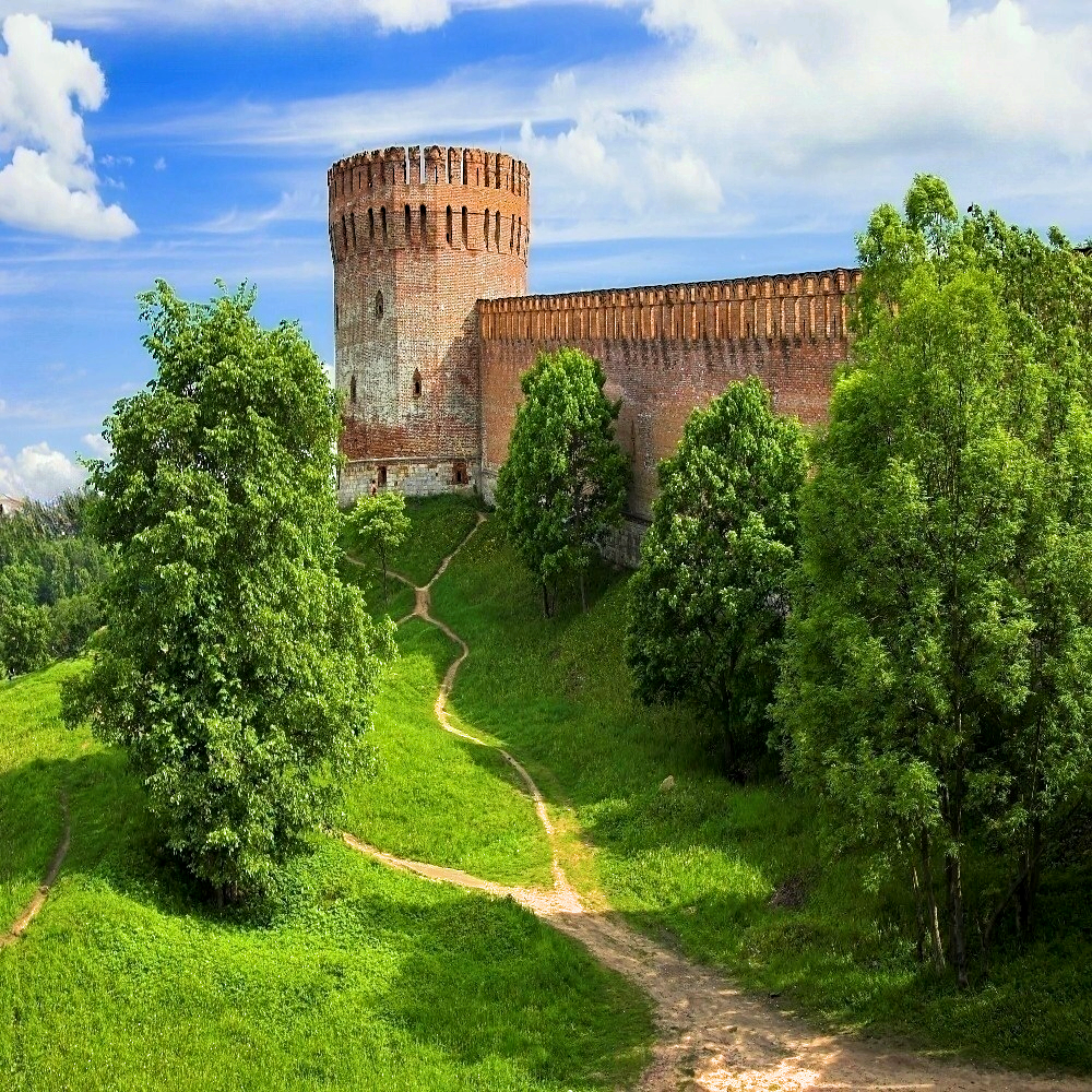 Массивные башни и кирпичная стена Смоленской крепости среди зелёных деревьев
