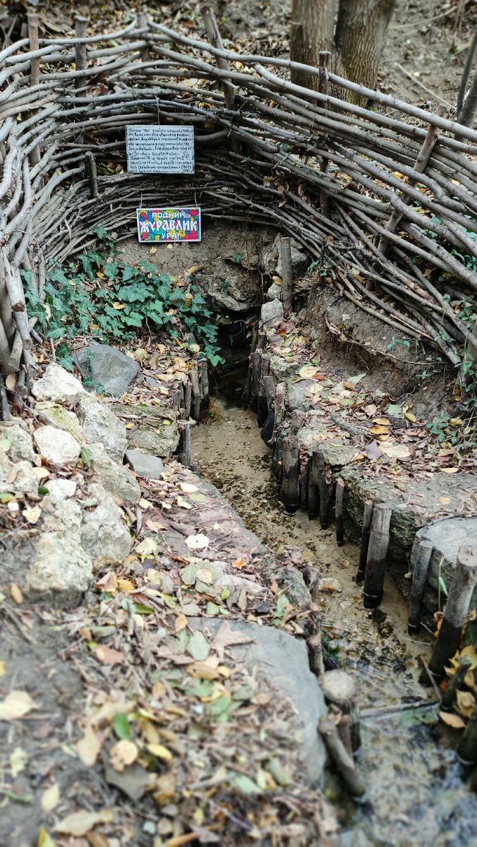 Окрестности этого родника выглядят по-настоящему природными: русло наполнено чистой холодной водой, берега укреплённый колышками из веток, устье родника огорожено плетëным заборчиком, а на берегах ручья природный камень