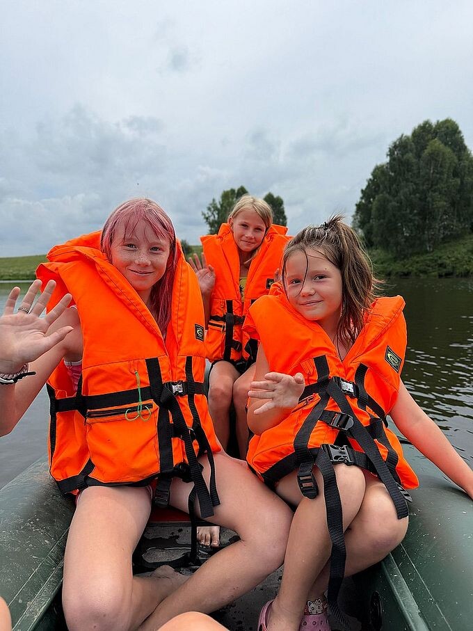 Три девочки в спасательных жилетах сидят в надувной лодке