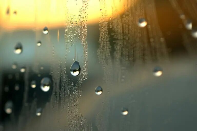 Запотевшее стекло с каплями воды. Такой конденсат часто образуется на деревянных окнах из-за разницы температур внутри и снаружи помещения и повышенной влажности воздуха.