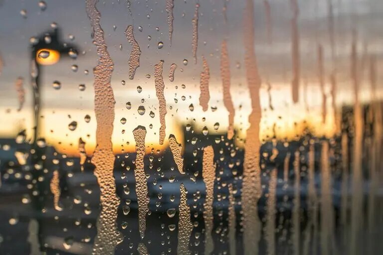 Запотевшее окно с крупными каплями воды, стекающими вниз. Такое запотевание характерно для деревянных окон при высокой влажности и перепаде температур между улицей и помещением.