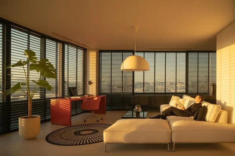 Просторная гостиная с панорамными окнами, на которых установлены горизонтальные жалюзи. Такой монтаж позволяет удобно регулировать освещённость и сохранять современный стиль интерьера.