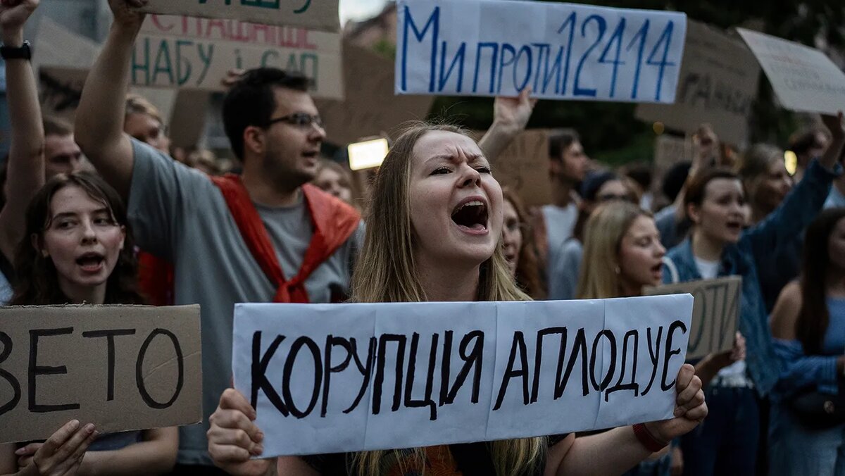   Alex Babenko / AP- Женщина, держит в руках плакат с надписью «Коррупция аплодирует» во время протеста против закона, направленного против антикоррупционных учреждений, в центре Киева, Украины