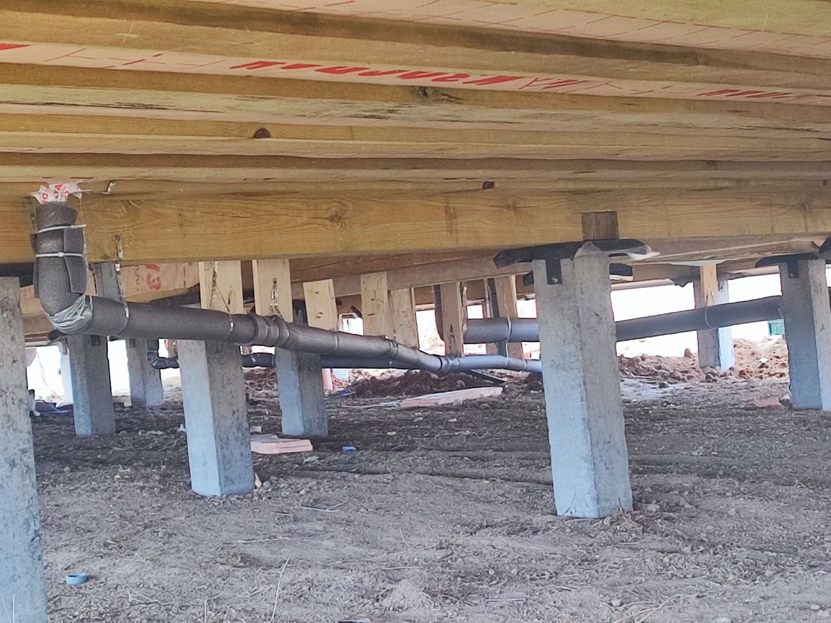 Прокладка и утепление канализационной трубы под каркасным домом на свайном фундаменте. Правильный уклон и теплоизоляция защищают систему от промерзания зимой. Фото с объекта «Интел Групп».