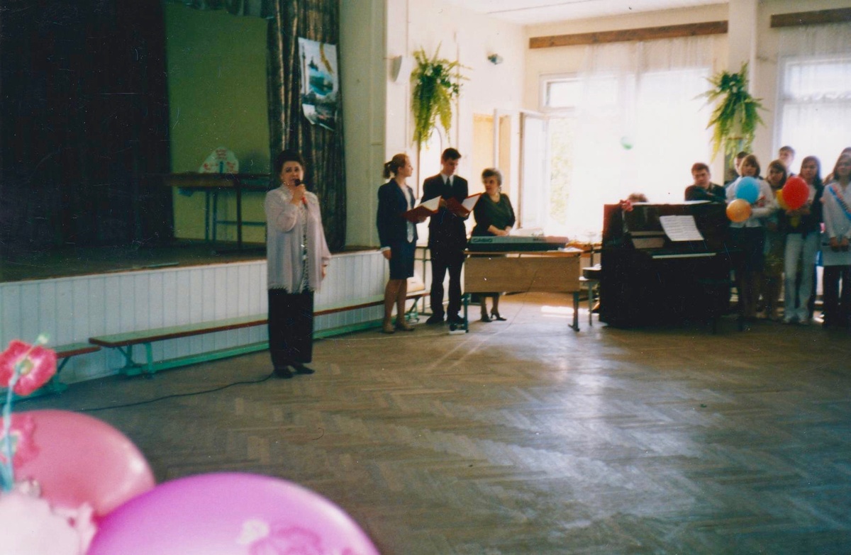 Вот она, директриса, с микрофоном — притворяется нормальным человеком