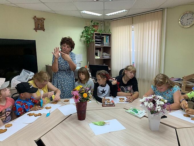 Дети за круглым столом слушают Сальцову Ларису Петровну и раскрашивают пряники