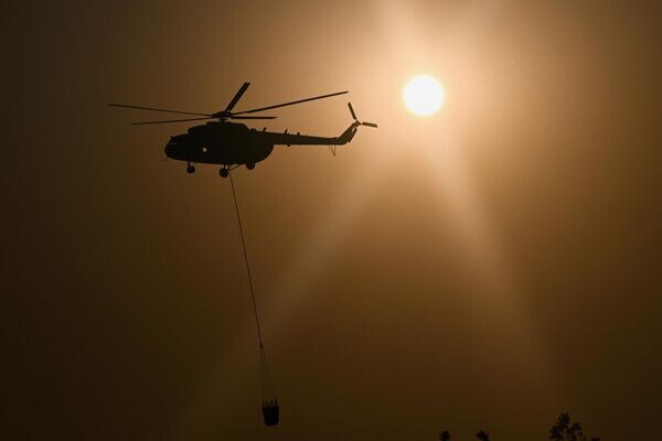 Пожарный вертолета на фоне заходящего солнца виден во время тушения лесных пожаров в районах Сафранболу и Оваджик в Карабуке (27 июля 2025). Турция