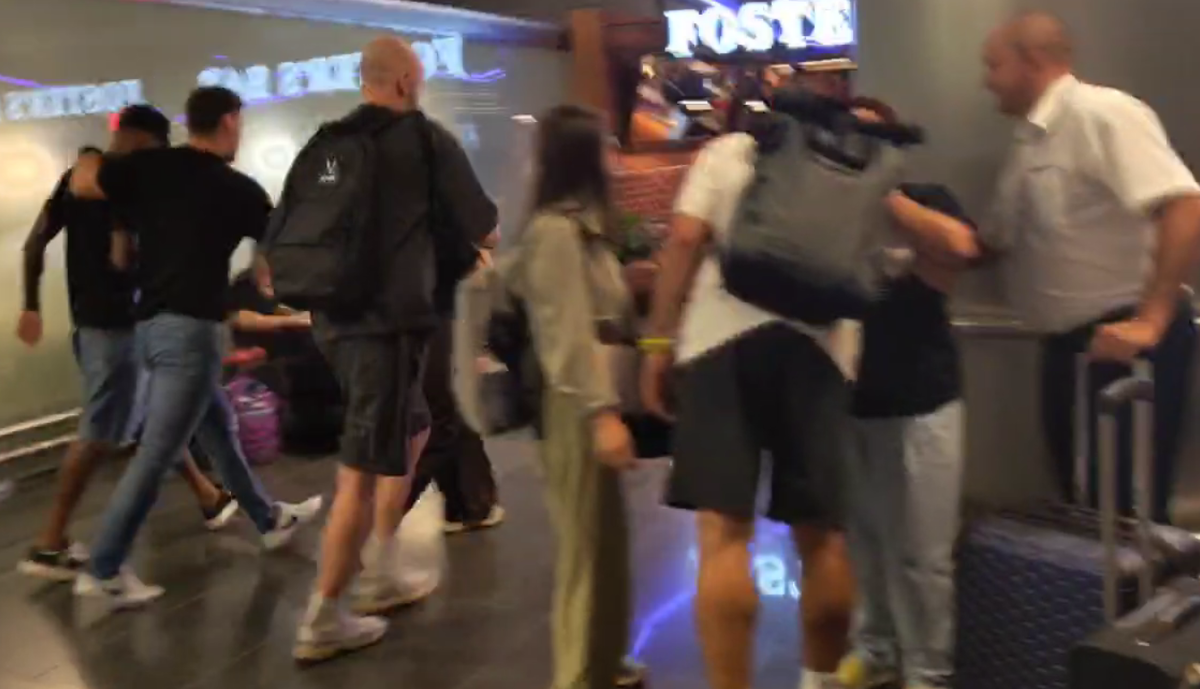 Жедсон (слева) под руки спешно направляется к выходу аэропорта, пряча голову