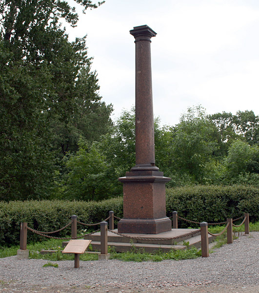 Современное фото Молвинской колонны в Екатерингофе, окутанной туманом, на фоне осенних деревьев.