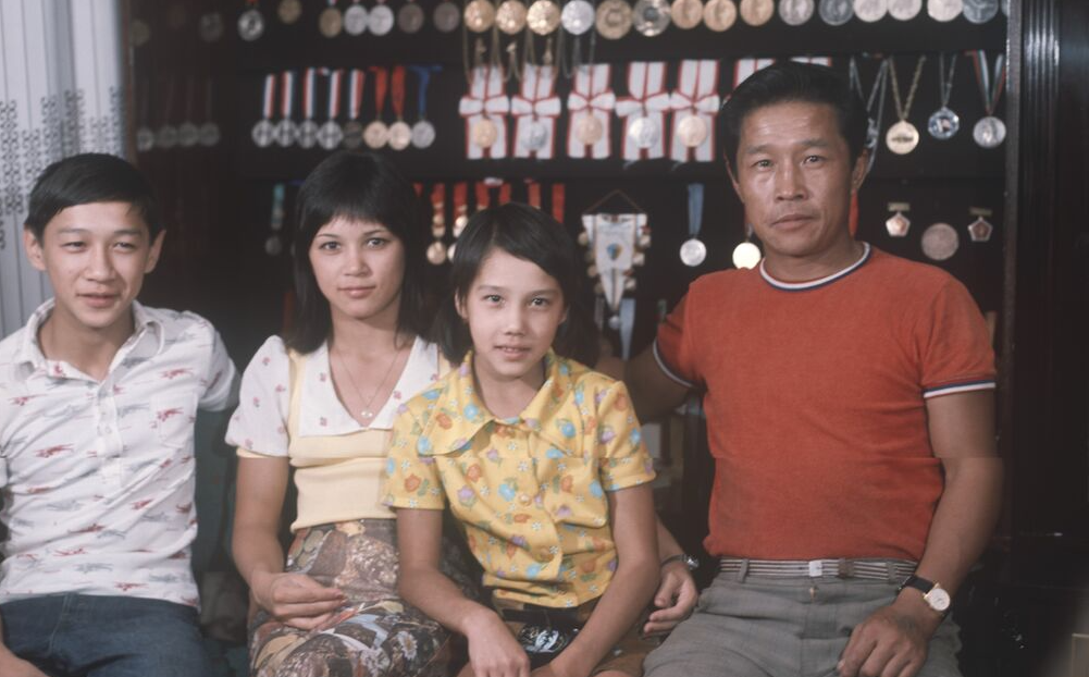 Гимнастка Нелли Владимировна Ким (1957 г. р.) с отцом, братом и сестрой на фоне своих спортивных наград, источник: Риа Новости