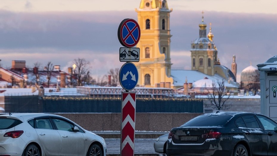    Дорожный знак запрета парковки и принудительной эвакуации транспорта на фоне припаркованных автомобилей и Петропавловского собора. Автор фото: Тихонов Михаил
