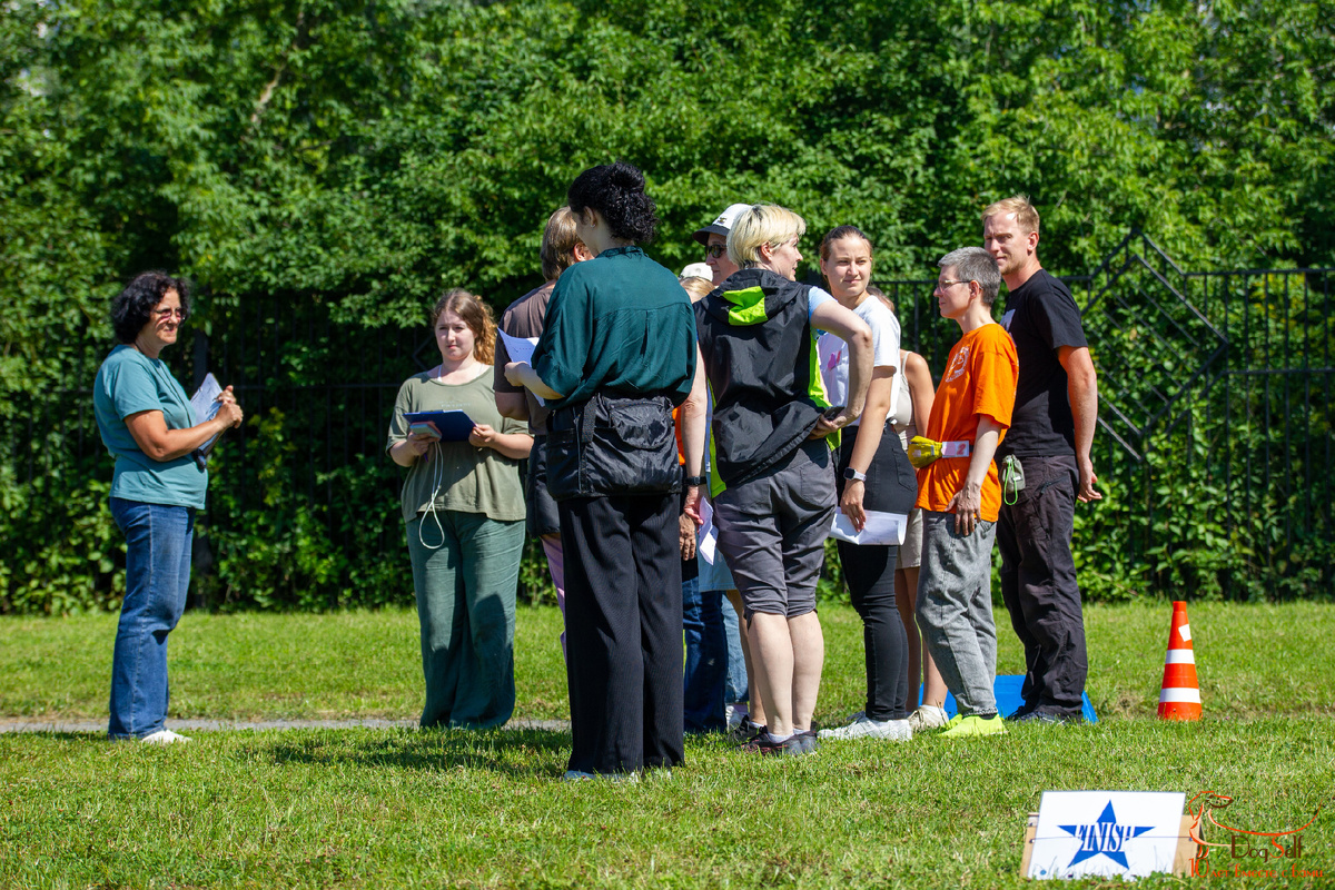 Общий план соревнований по Ралли Обидиенс в КЦ DogSelf, Москва, КСК «Битца». Судейская команда, участники и волонтёры на удобной зелёной поляне. Фото: Алиса Пономарёва, специально для DogSelf.