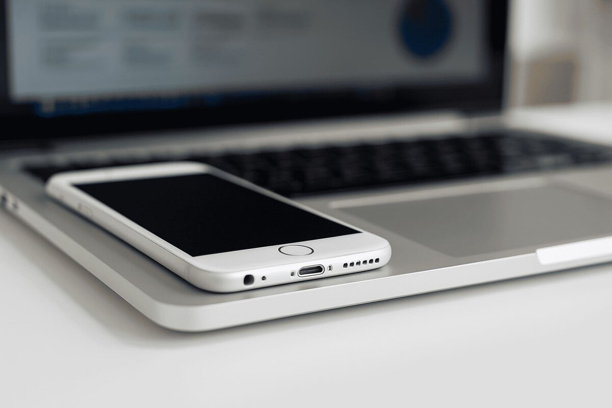 Смартфон лежит на клавиатуре ноутбука с включенным экраном.