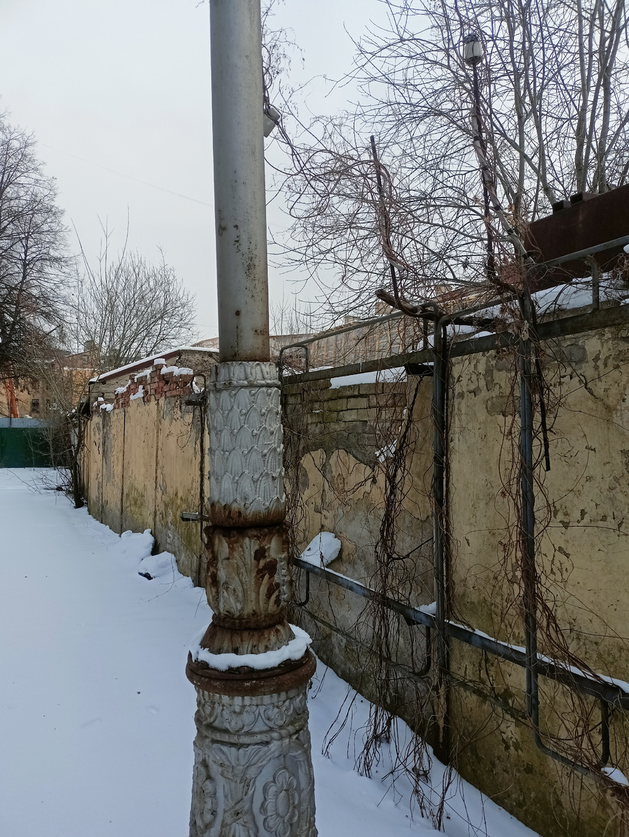 В итоге основной фасад смотрит на глухую, покосившуюся стену и старые ржавые, но очень изысканные, некогда, мачты фонарей.