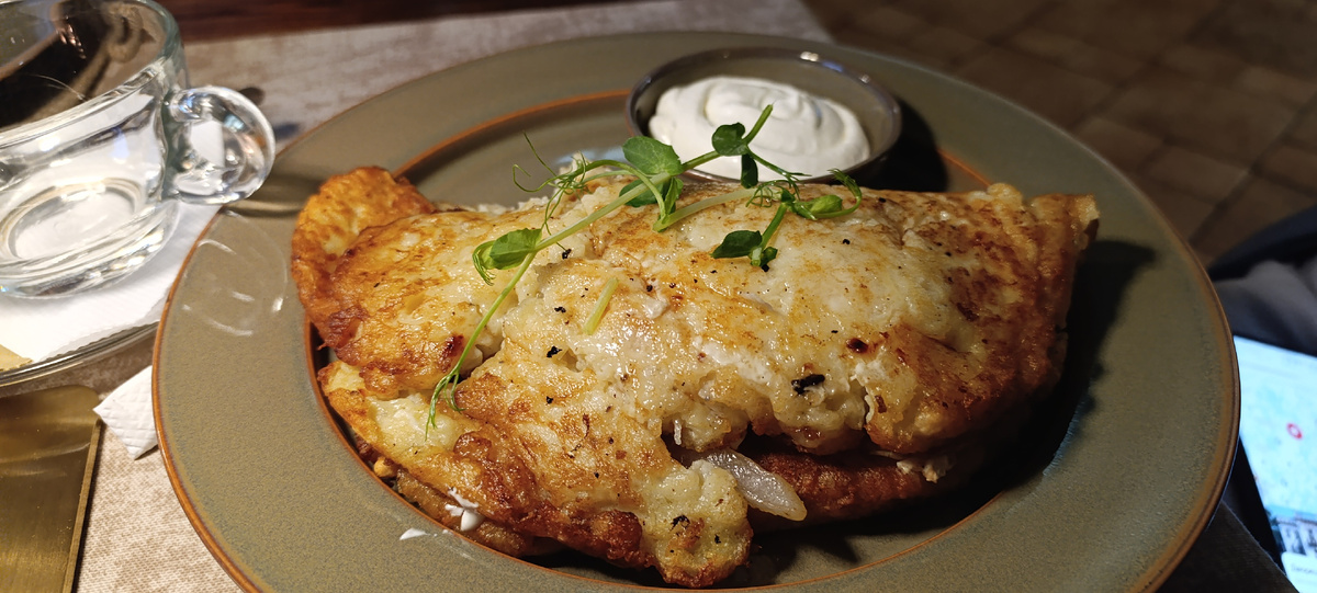 Это драник с ветчиной, луком и жареным яйцом внутри, со сметаной, в которой ложка стоит, тарелка просто огромная, и холодник с картофельными дольками. Наша благодарность за обслуживание - обязательно.