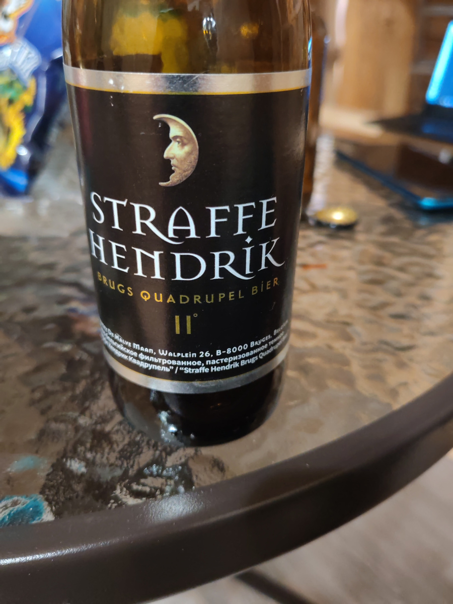 Это Straffe Hendrik Brugs Quadrupel Bier 11° — крепкий бельгийский тёмный эль (quadrupel) из Брюгге, пивоварня De Halve Maan. Крепость около 11%: насыщенное, тёмно‑рубиновое, с ароматами сухофруктов (изюм, инжир, чернослив), карамели и тёмного сахара, пряностями бельгийских дрожжей (гвоздика, перец), легкими нотами шоколада/ликорицы; горечь умеренная, финал тёплый и суховатый. Подавайте при 10–12°C в бокале тюльпан/келих, наливать стоит аккуратно (возможен небольшой осадок). Хорошо сочетается с выдержанными сырами (особенно блю и гауда), томлёной говядиной, дичью, а также десертами с тёмным шоколадом. Марка «Straffe Hendrik» (в переводе «Крепкий Хендрик») названа в честь династии пивоваров семьи Maes; фирменная «луна» — символ пивоварни из Брюгге. Многие партии неплохо выдерживаются 2–5 лет в прохладе, вкус становится более винным и округлым.