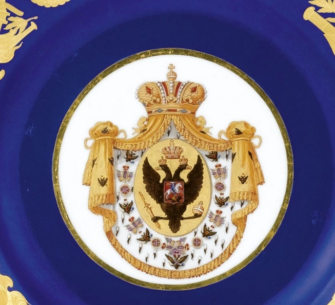 Основной рисунок на зеркале тарелки: герб Российской империи в виде двуглавого орла с соответствующими атрибутами (скипетр, держава, короны, герб Москвы) на золотом фоне, заключённый в овал, расположенный на белой горностаевой мантии в обрамлении ещё одного геральдического символа Российской империи — цепи ордена св. Андрея Первозванного. Фото: Порцелиновый фан / dzen.ru, https://vk.cc/cywZax
