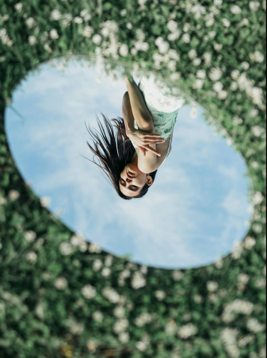 Отражение женщины в зеркале на фоне природы — словно кадр из художественного фильма, нежный и визуально тёплый.