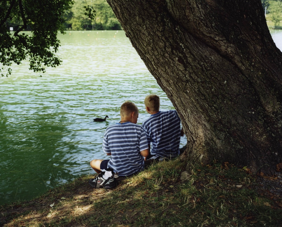Близнецы сидят на берегу Женевского озера в Лозанне, Швейцария. Исследования показывают, что синхронное поведение, часто наблюдаемое у близнецов, обусловлено общей генетикой и схожим жизненным опытом, а не телепатической связью.