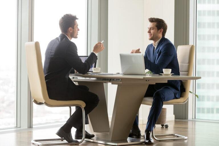    Two handsome businessmen sitting in comfortable chairs at desk with laptops in meeting room. CEO making important negotiation about companies partnership or corporate merger. Financiers planning deal Артем Силантьев