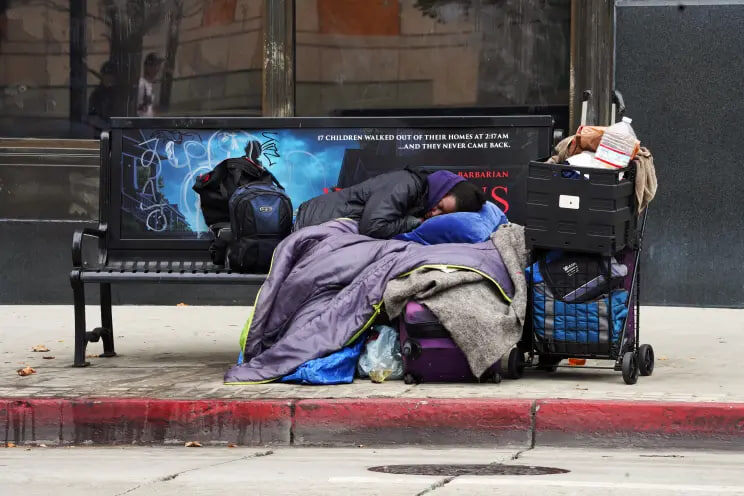 Бездомный спит на скамейке на автобусной остановке.