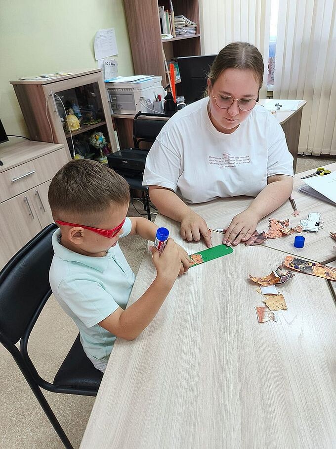 Дудникова Юлия Александровна помогает мальчику наклеить аппликацию