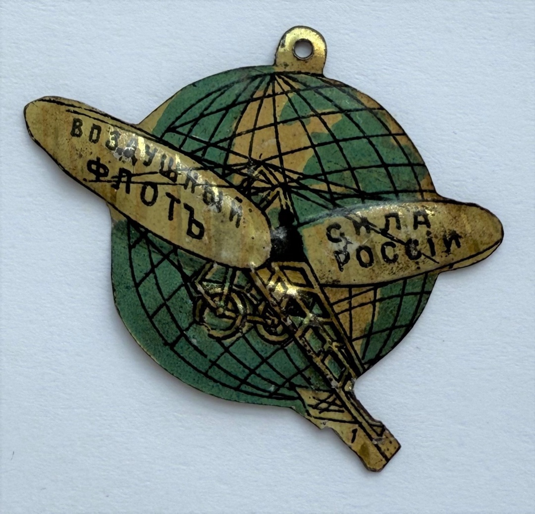 ОГС КП-335
Жетон представляет собой земной шар с параллелями и меридианами, по которому летит аэроплан. На левом крыле надпись: «ВОЗДУШНЫЙ ФЛОТЪ», на правом крыле «СИЛА РОССIИ». Название фабрики-изготовителя на оборотной стороне: «ФАБРИКА М. КОКА и М. БИРМАНЪ С.П.Б».