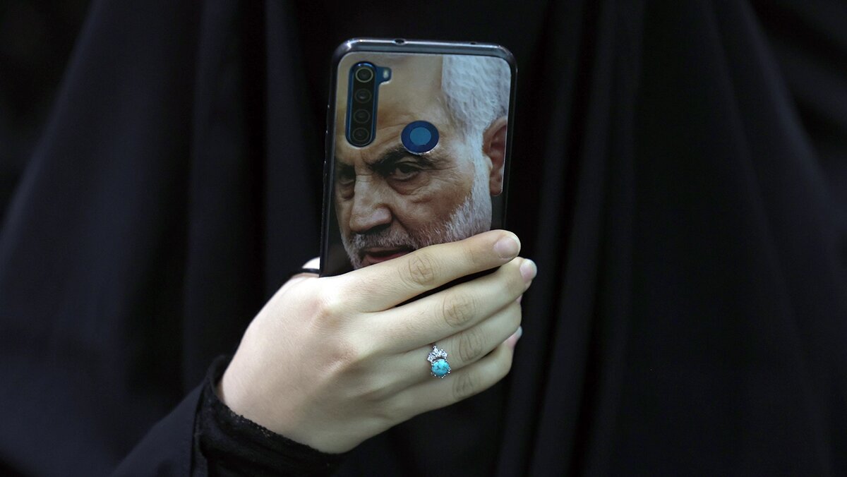   Abedin Taherkenaren / EPA / TASS- Иранская женщина держит телефон с изображением покойного командующего спецподразделением КСИР Касема Сулеймани. Тегеран, Иран, 2 января 2025 года