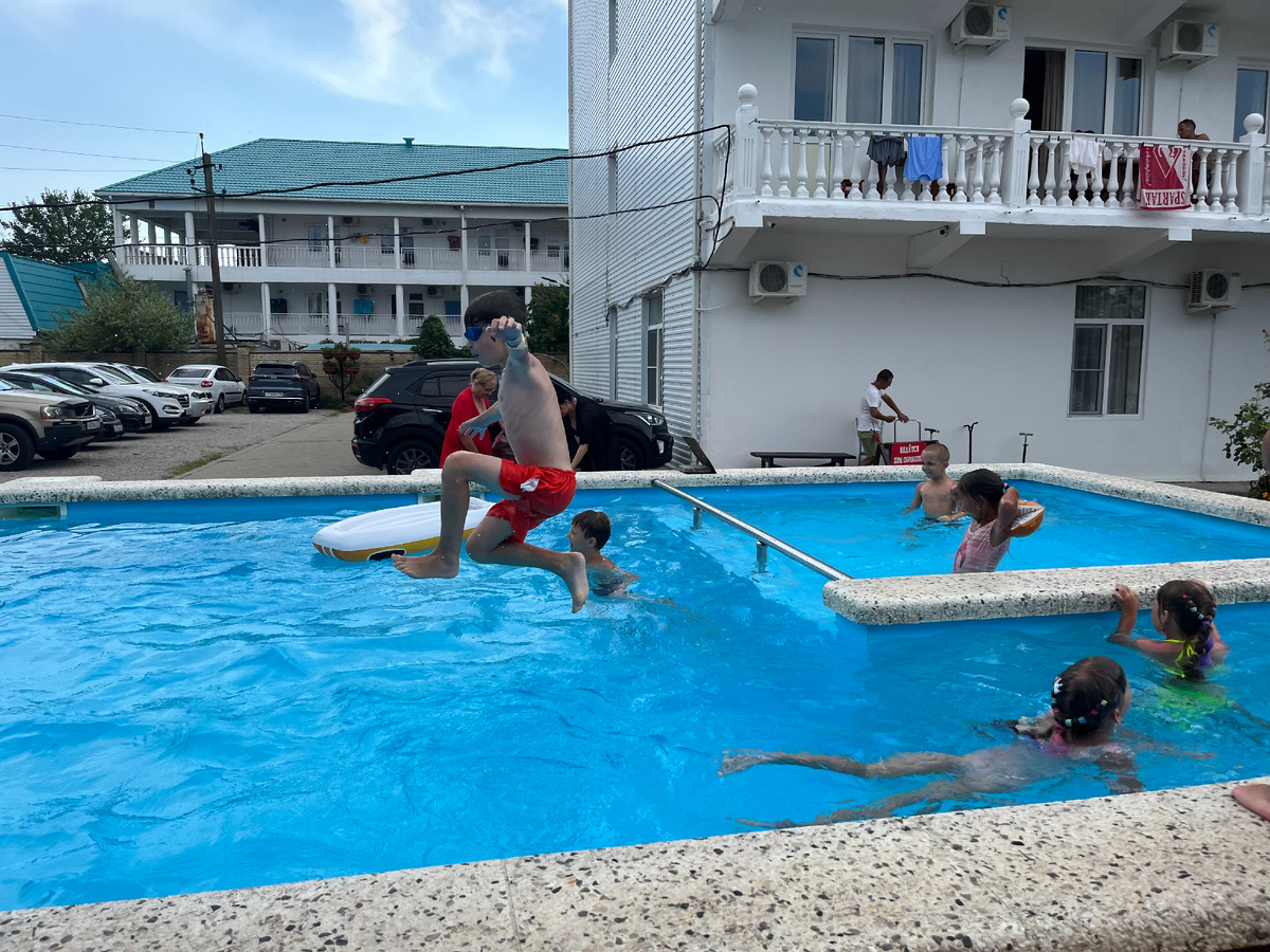 дети веселятся в бассейне, за кадром отдыхают взрослые