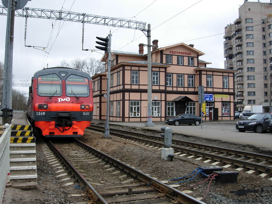 Здание железнодорожного вокзала Сестрорецк, вид с пешеходного перехода, и электропоезд ЭД4М-0411 на фоне вокзала. Старый карликовый светофор вскоре будет заменён на новый, мачтовый. Его головка пока повёрнута в сторону от пути. Фото.2015 г.