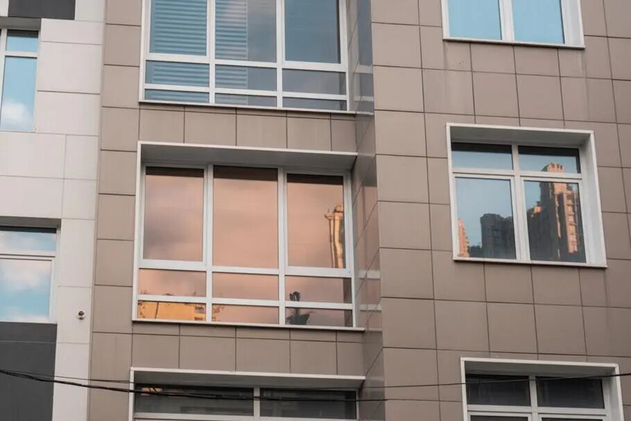 Фасад современного дома с окнами, часть из которых имеет зеркальную тонировку. Такое решение защищает помещение от лишнего солнечного света и повышает приватность.