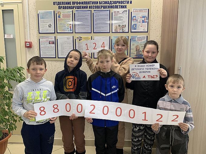 Группа детей держат листы с надписью детского телефона доверия