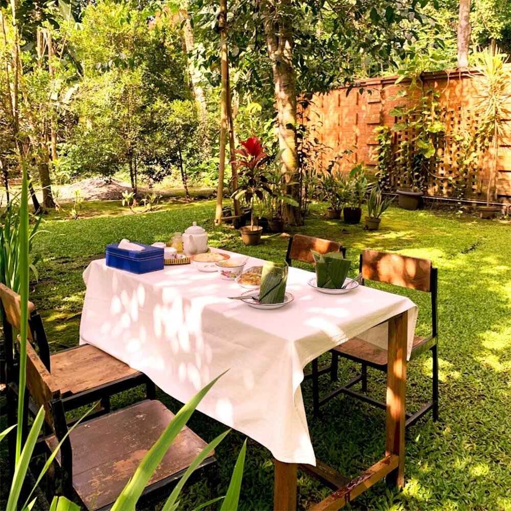 Утренний стол на газоне: backyard работает как продолжение столовой. Трава - фон, по периметру горшечные растения и тень от деревьев.