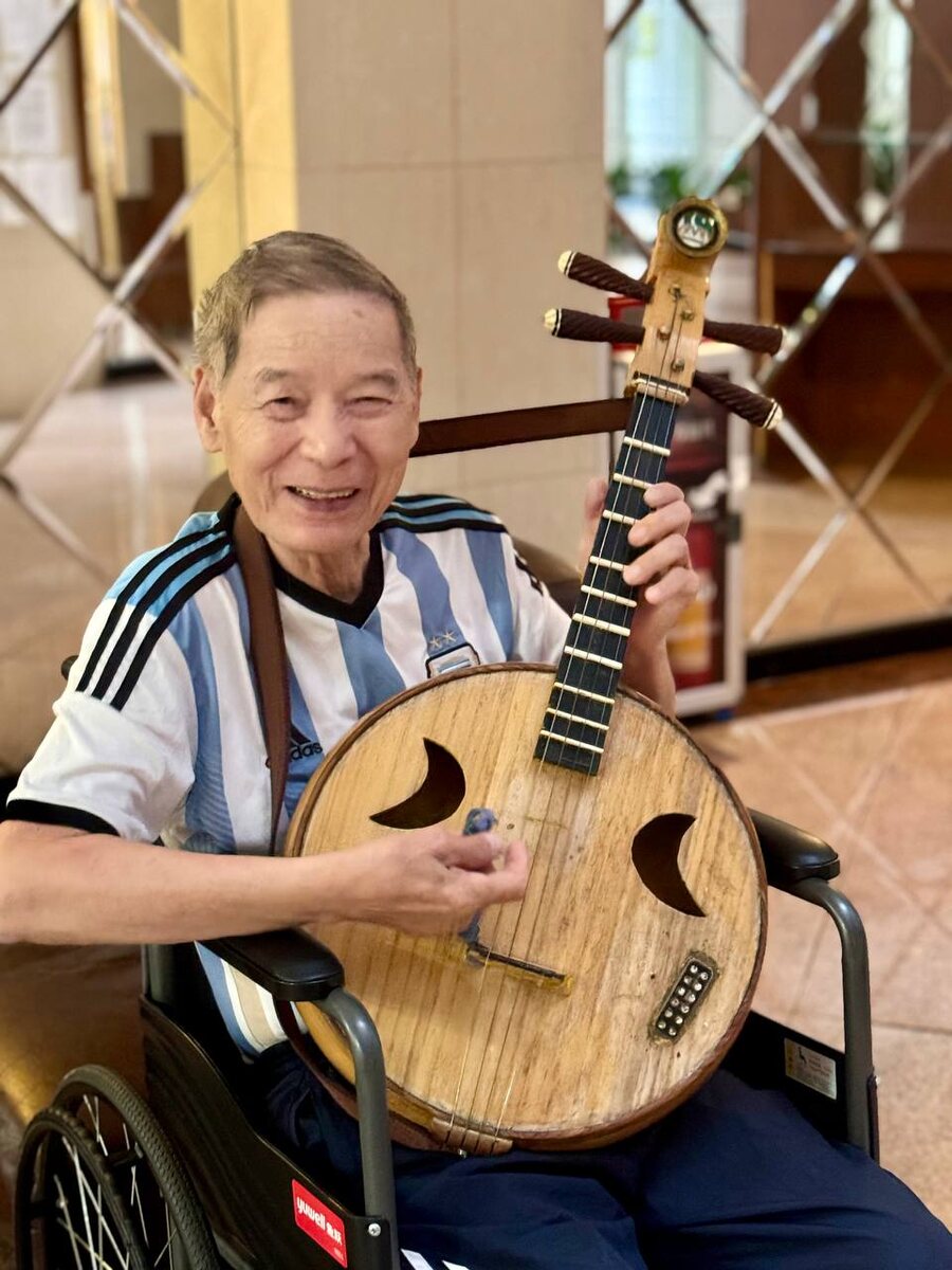 Пенсионер в инвалидной коляске в подъезде дома играет на популярном в Китае национальном музыкальном инструменте жуань, центр Гуанчжоу