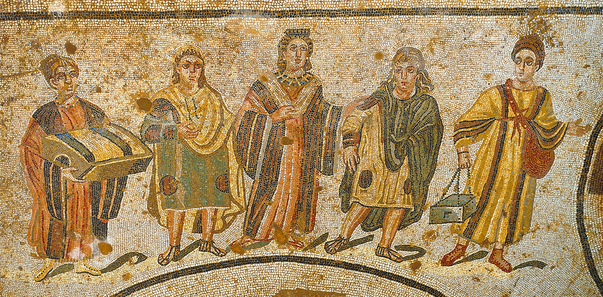 Элегантность в римском платье
С первого века римская мода для женщин стала гораздо более разнообразной, впитывая веяния с Востока и из "варварских" земель. Цвета, которые раньше редко встречались (зеленый, синий, фиолетовый), обрели новую популярность. Со временем даже мужчины стали носить оттенки, которые ранее считались неуместными. Эта напольная мозаика с роскошной сицилийской виллы иллюстрирует эти модные сдвиги, изображая хозяйку дома, направляющуюся в термы в ярком и пестром наряде. Ее сопровождают дочери в зеленом и желтом, а также две служанки, несущие, по-видимому, ткани и косметику.
Мозаика найдена в вестибюле виллы Романа-дель-Казале, недалеко от города Пьяцца-Армерина, Сицилия, первая четверть IV века.