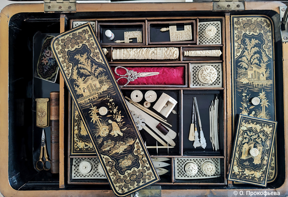 Столик для рукоделия. Вид внутри. Челноки, различные держатели в том числе и «третья рука», крючки, шило, всевозможные катушки для ниток и среди них затерялись игровые фишки из перламутра, игольницы, футляры для швейных принадлежностей, ножницы.