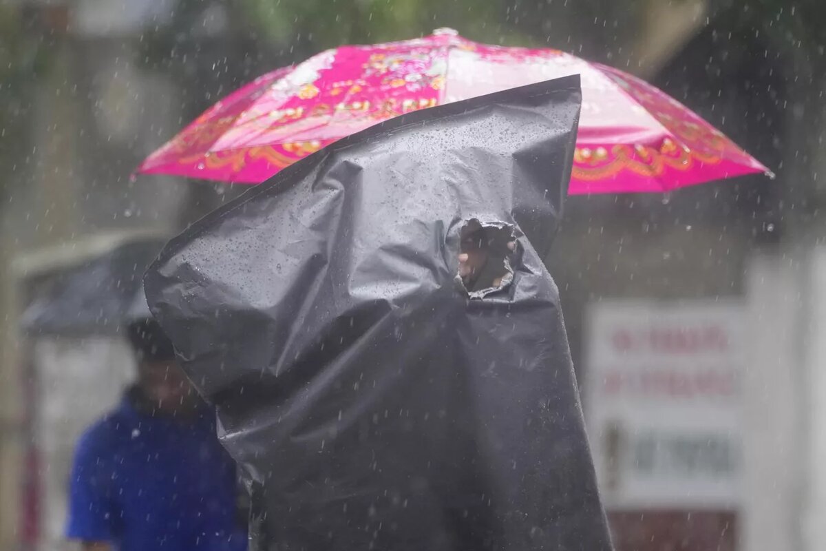 Мужчина, прикрываясь пластиковым чехлом, прогуливается во время сильного дождя