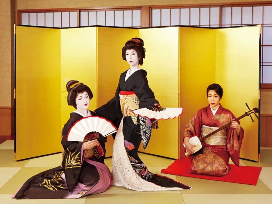 Две гейши танцуют, сзади – старшая гейша с сямисэном